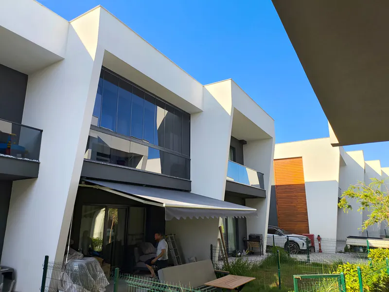 Beyaz modern binanın önünde gri mafsallı tente uygulaması – ANT BRANDA